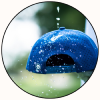 A circular close-up of a blue, water-dripped object, likely a decorative dome or container, set against a green background with blurred droplets.
