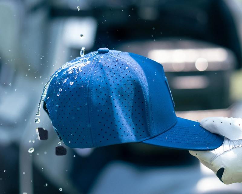 Blue cap with water droplets held by a gloved hand against a blurred background